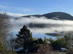 Um lago sereno com uma colina arborizada ao fundo e um céu claro.