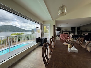 A dining area with a view of a lake and mountains, a fireplace, and a kitchen in the background.