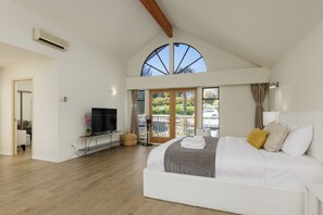 A spacious bedroom with a large bed, a flat-screen TV, and a balcony with a view of greenery.