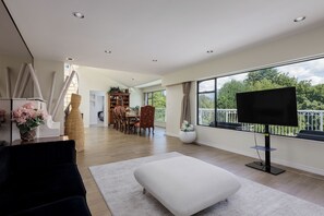 Un salon spacieux doté d’une grande fenêtre, d’un téléviseur à écran plat et d’un coin repas avec des chaises et une table.