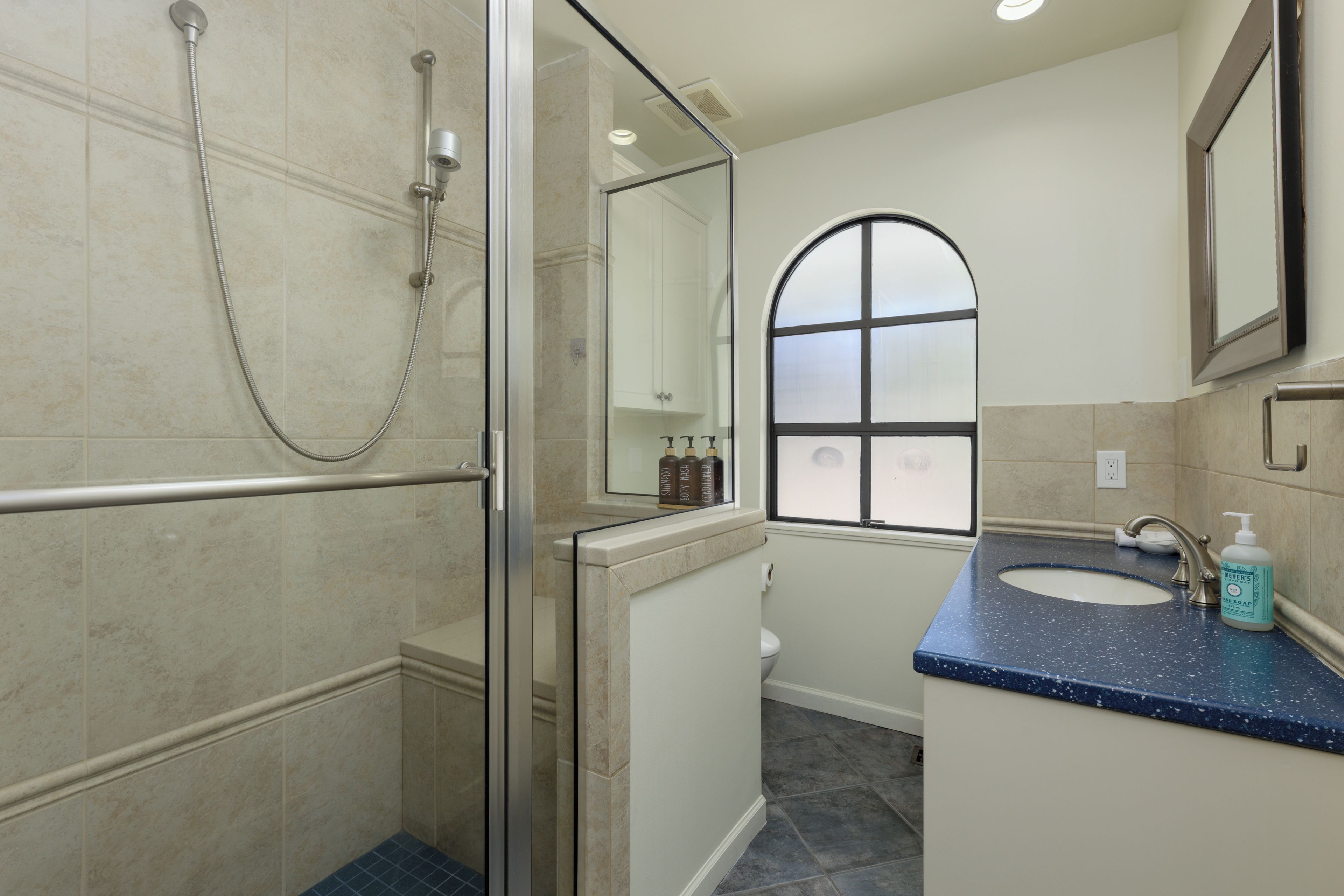 Une salle de bain dotée d’une douche à paroi de verre, d’un lavabo avec un plan de toilette bleu et d’une fenêtre en verre dépoli.