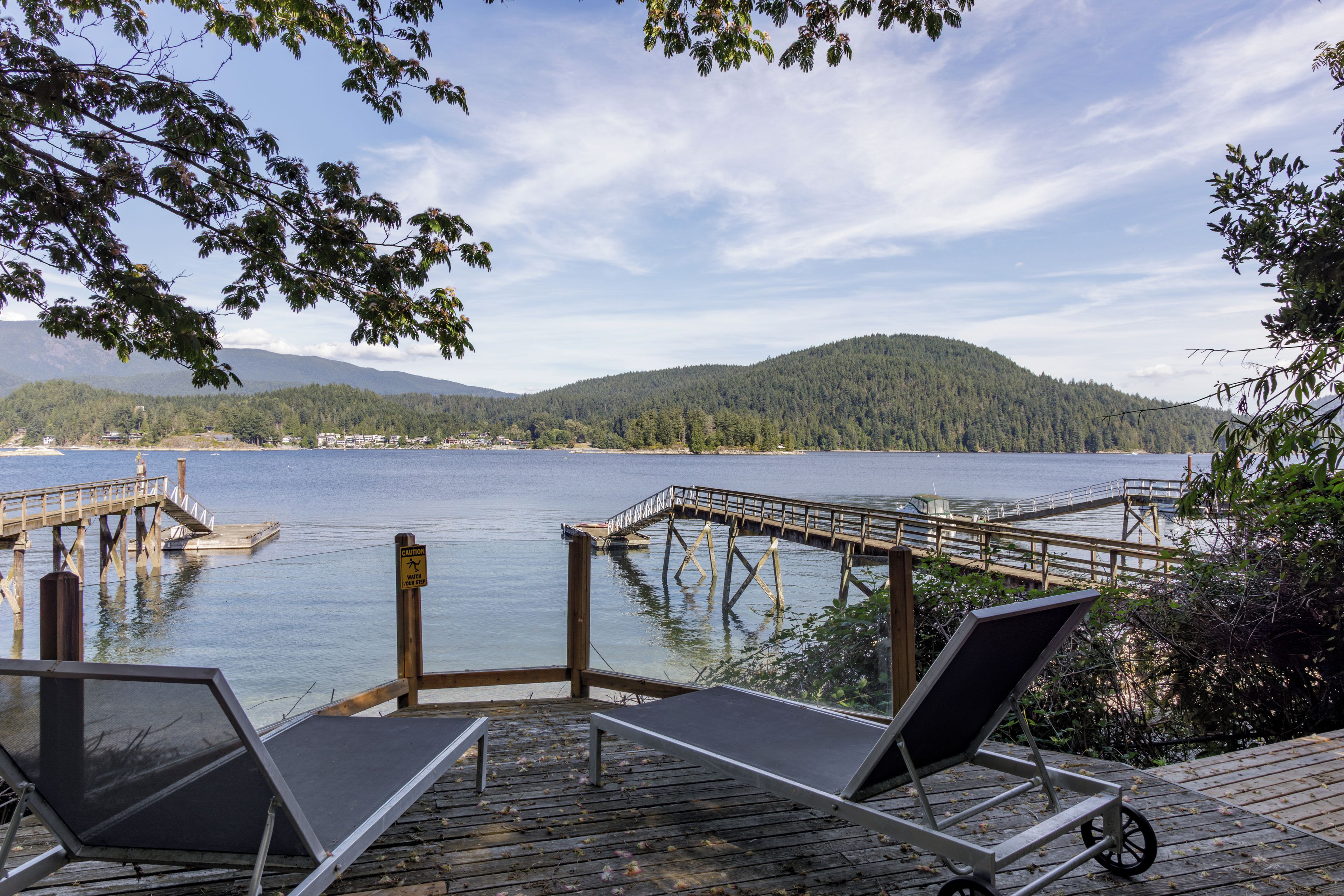 A lakeside deck with two lounge chairs, a wooden dock, and a caution sign.