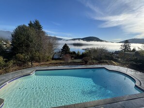 Piscina transparente com vista para um lago e montanhas ao fundo.
