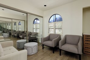A modern living room with a large mirror, two armchairs, a round ottoman, and a glass coffee table.