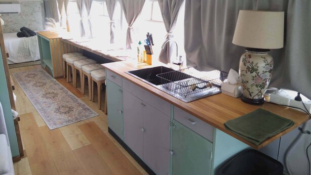 A compact kitchen with a wooden countertop, a sink, and a dining area with stools. - Vintage Bedford Bus Farm Glamping Under the Stars (Silverwood)