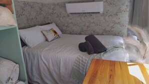 A neatly made bed with a floral headboard, a pillow with a sunflower design, and a wooden bedside table. - Vintage Bedford Bus Farm Glamping Under the Stars (Silverwood)