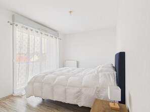 A bedroom with a bed, a bedside table with a lamp, a radiator, and a window with curtains. - Apartment for 4 in the heart of La Baule (La Baule-Escoublac)