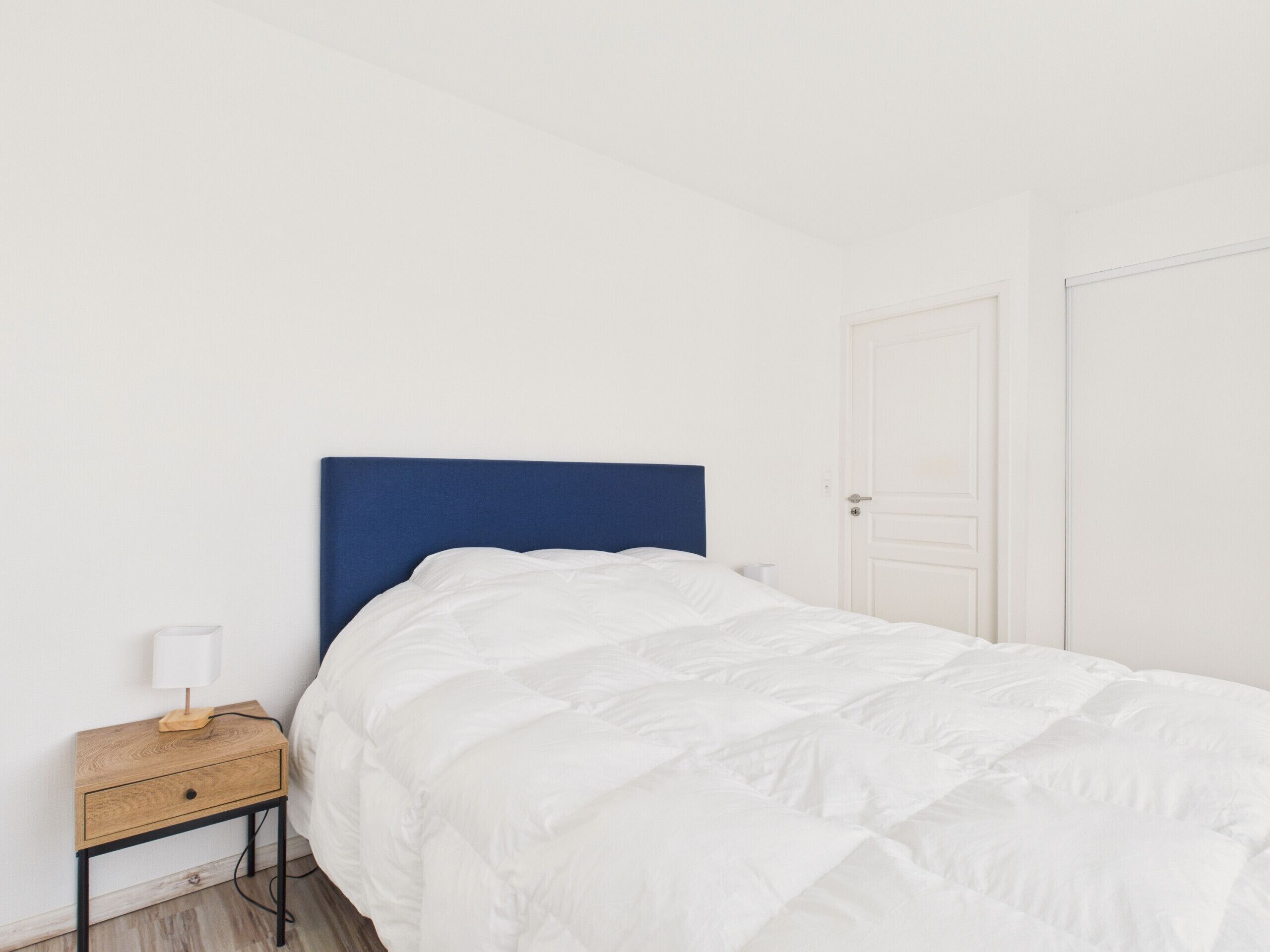 Un dormitorio con una cama individual, una mesita de noche con lámpara y una puerta cerrada.