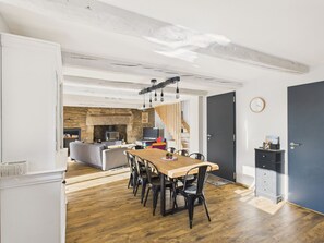 A modern kitchen with a stone wall, wooden flooring, and a dining area with a wooden table and chairs. - City center – Large house for 10 with garden (Ploemel)