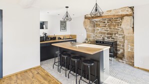 A modern kitchen with a central island, bar stools, a stone fireplace, and pendant lighting.
