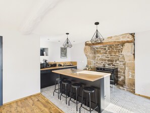 A modern kitchen with a central island, bar stools, a stone fireplace, and pendant lighting. - City center – Large house for 10 with garden (Ploemel)