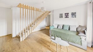 A modern living room with a wooden staircase, a sofa with cushions, a small table, and wall art.