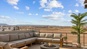 A modern outdoor seating area with a fire pit, a large cushioned sectional sofa, and a potted palm tree. - Terra Rossa: Desert Color Lagoon  + Beaches (St. George)