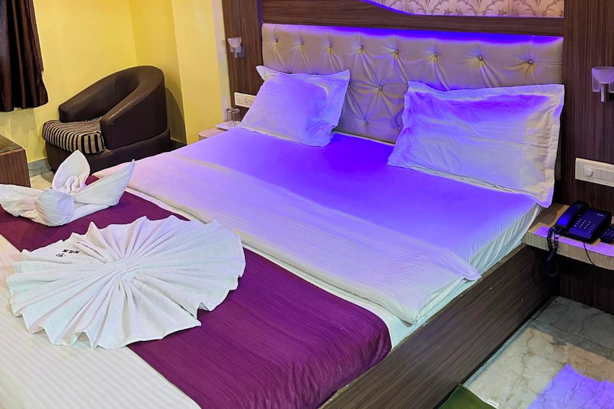 A hotel room with a large bed, a headboard with decorative lighting, a small seating area, and a ceiling fan.