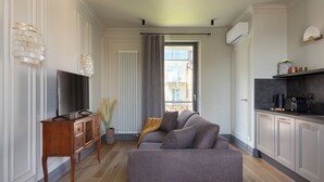Een moderne woonkamer met een grijze bank, een houten tv-meubel en een groot raam met gordijnen.