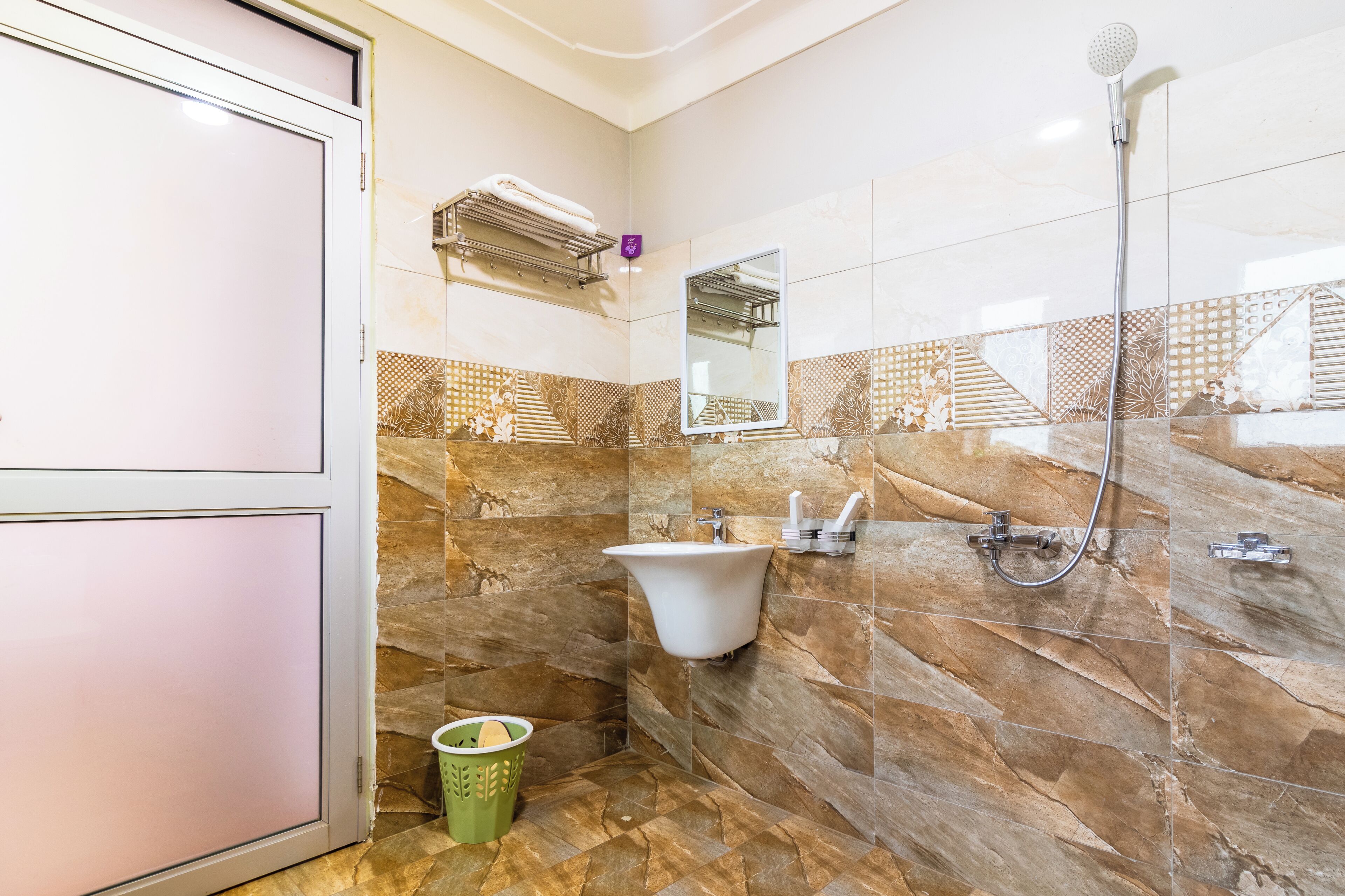 Un baño con pared de mármol, un lavamanos, un espejo, una ducha y un perchero para toallas.