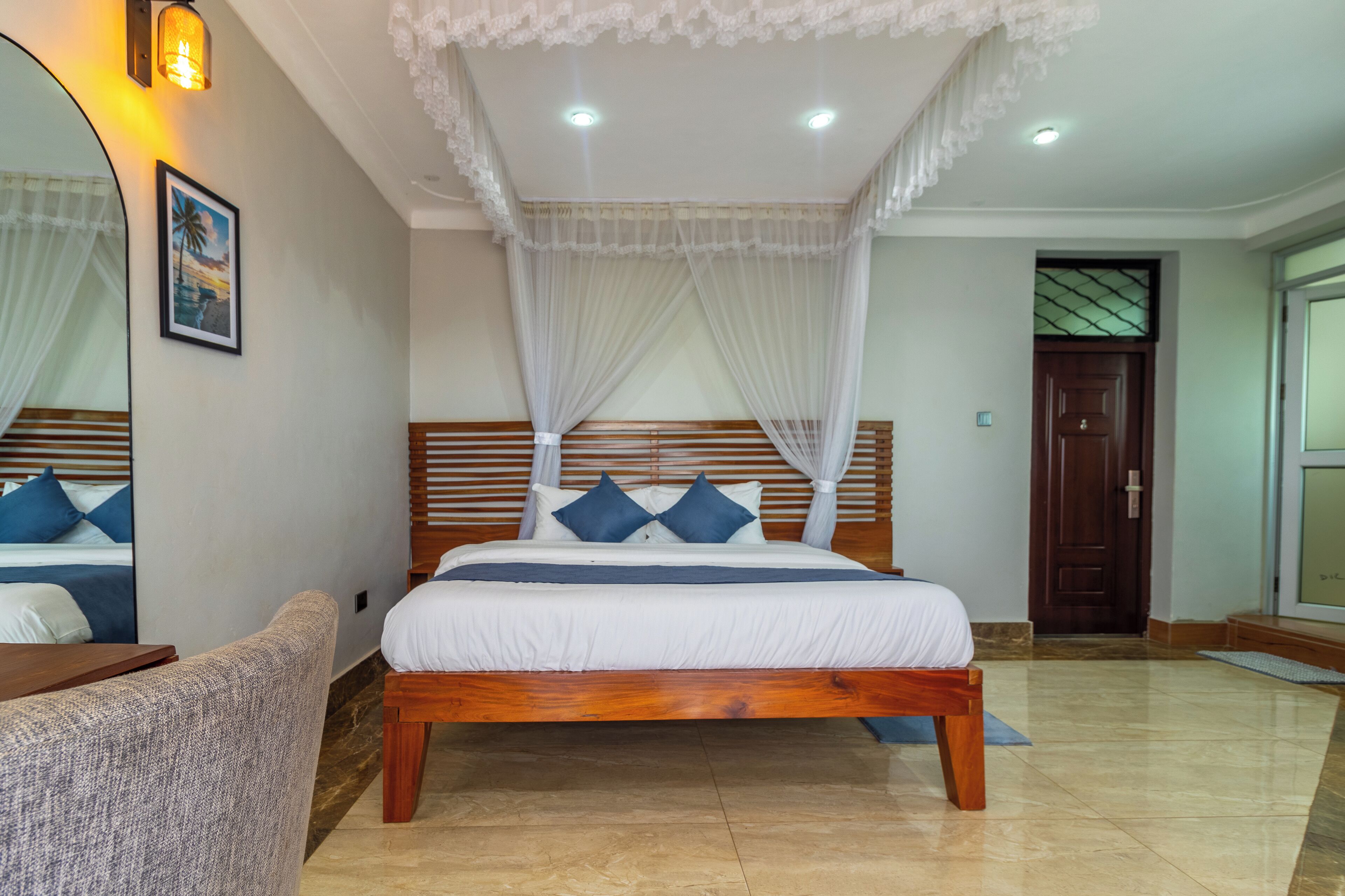 A bedroom with a wooden bed, white bedding, a canopy, a nightstand, a chair, and a large mirror.