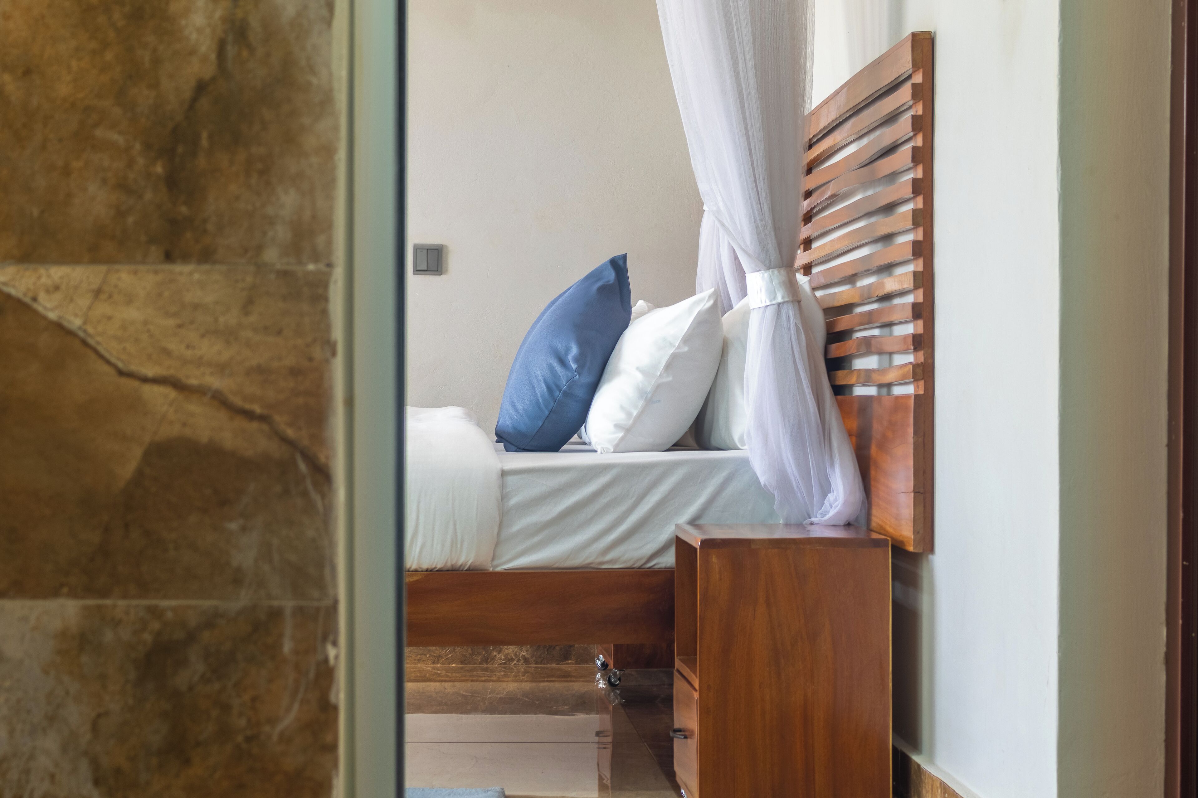 Een slaapkamer met een bed, witte beddengoed, een houten hoofdbord en een witte hemel.