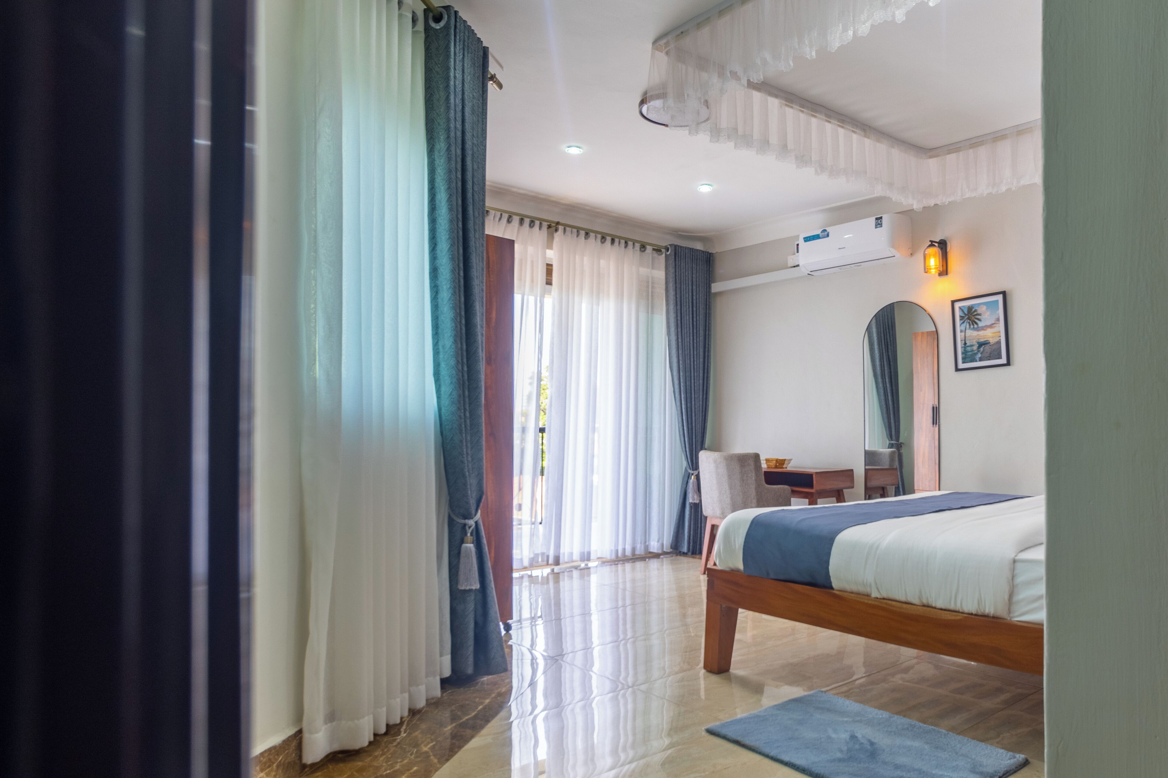 Une chambre d’hôtel avec un lit, un bureau, une chaise, un miroir et une fenêtre avec des rideaux.