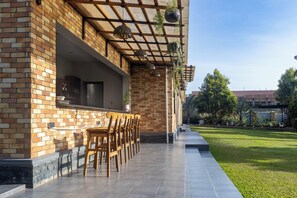 Un espace patio agrémenté d’un mur en briques, de chaises en bois, de jardinières suspendues et offrant une vue sur une pelouse verdoyante et des arbres.