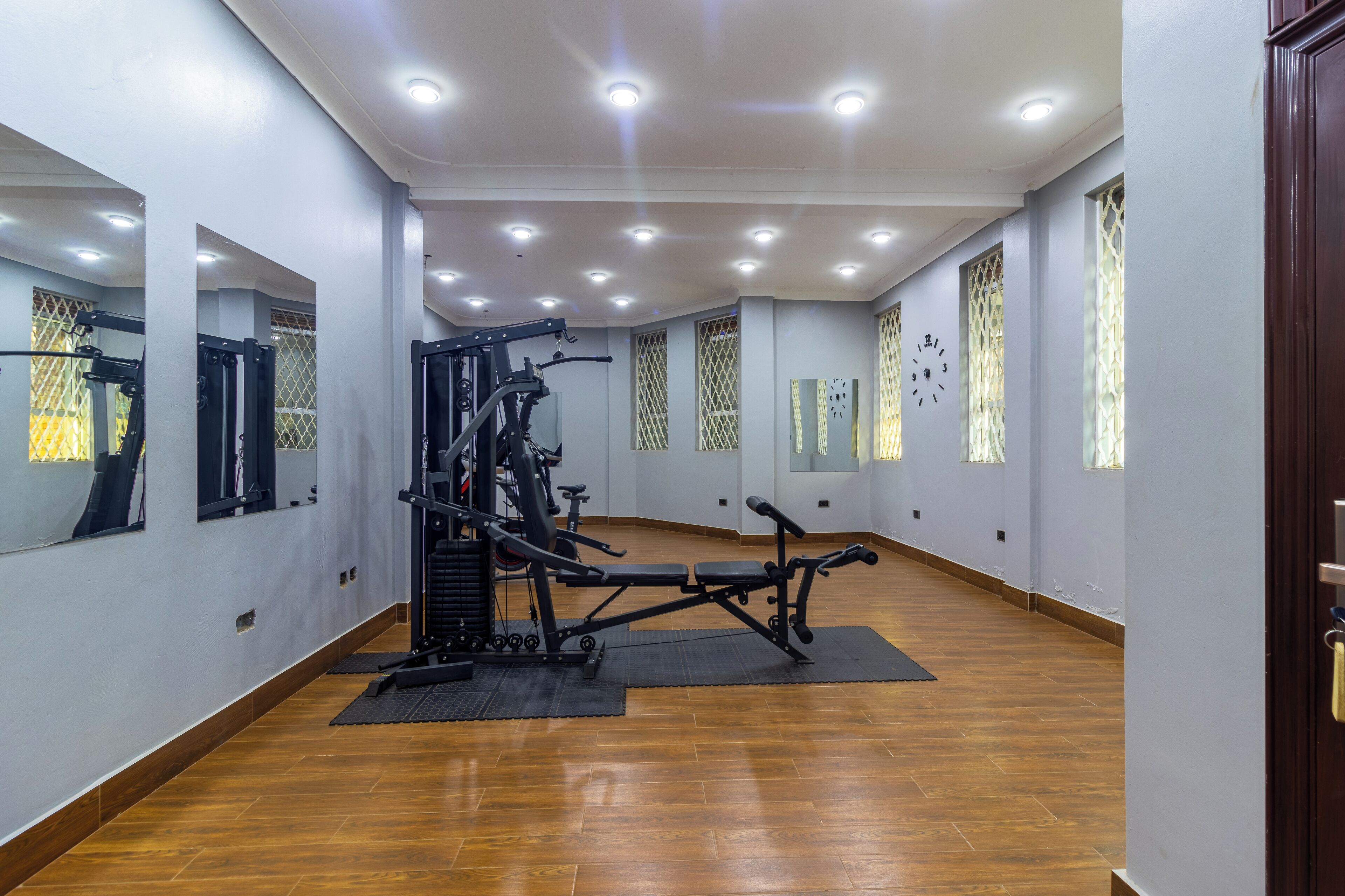 A gym with exercise equipment, wooden floors, and large windows with patterned curtains.