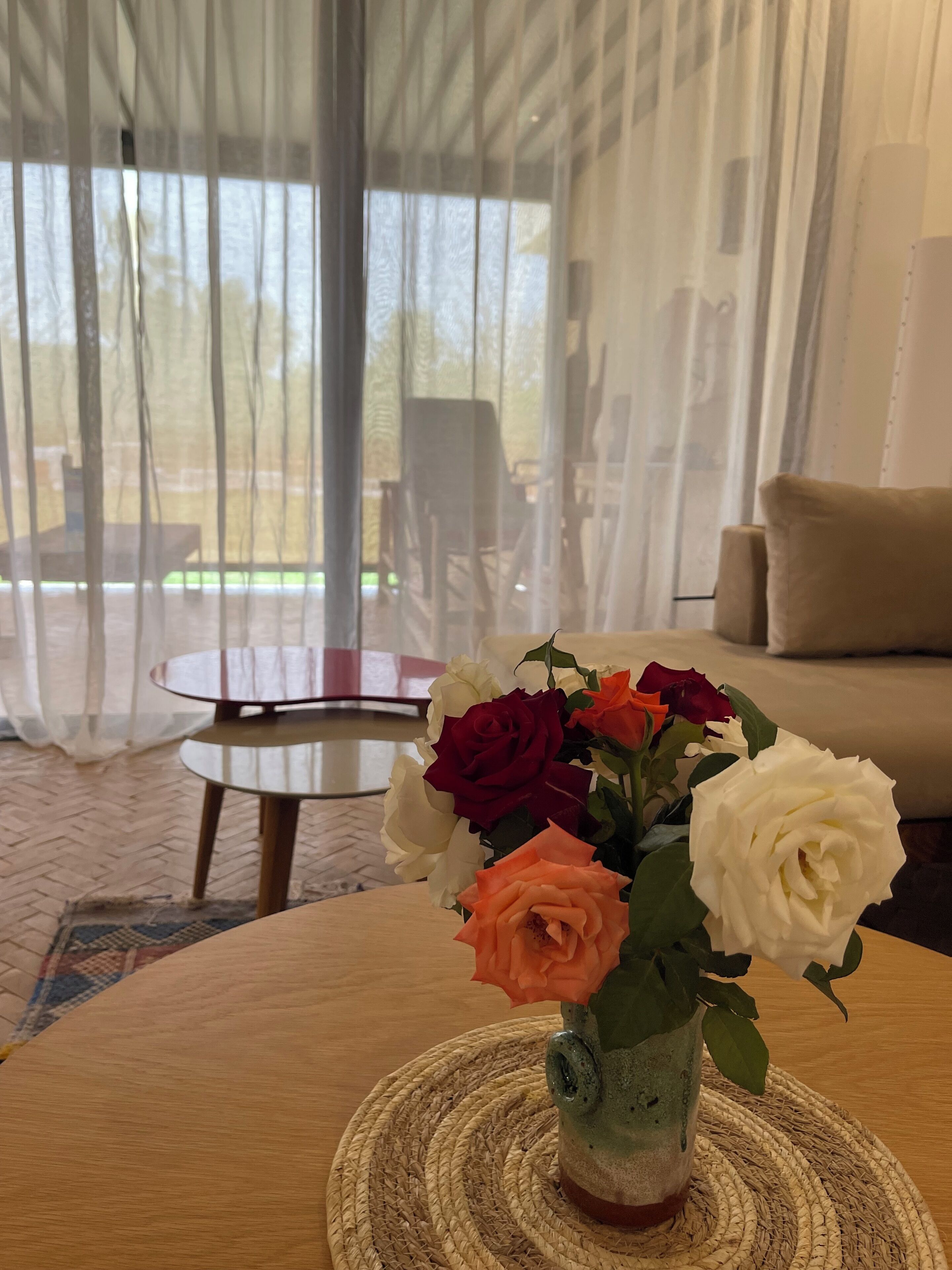 A room with a round wooden table, a woven placemat, and a vase with roses.
