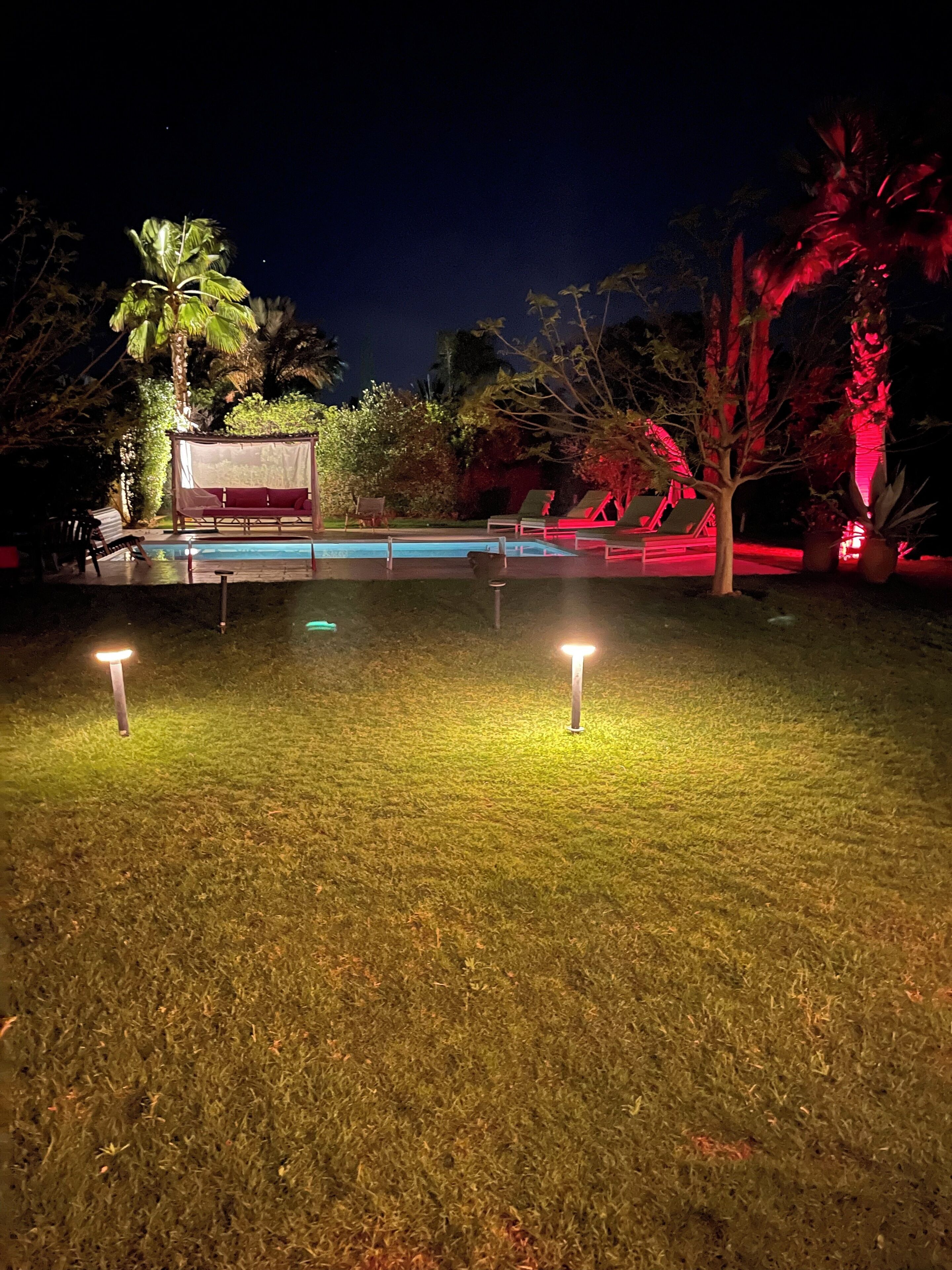 Ein Außenbereich bei Nacht mit Pool, Liegestühlen und einer überdachten Sitzgelegenheit.