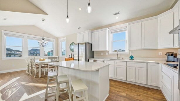 A spacious kitchen with white cabinetry, a central island, and a dining area with chairs. - Brand New Semi-Oceanfront Waves Home with Private Pool, Hot Tub, and Elevator (Waves)