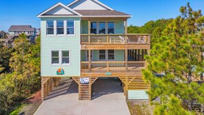 A two-story house with a balcony, a garage, and a sign indicating a surfboard rental. - Brand New Semi-Oceanfront Waves Home with Private Pool, Hot Tub, and Elevator (Waves)