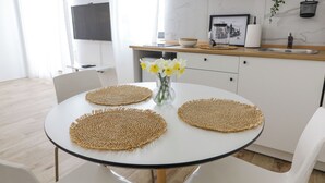 A modern kitchen with white cabinetry, a round dining table with woven placemats, and a vase of yellow flowers.