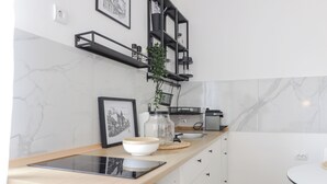 A modern kitchen with white marble walls, a wooden countertop, and black shelving units.