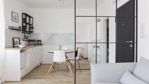 A modern kitchen with white cabinets, a dining area with a round table and chairs, and a grey sofa in the foreground.