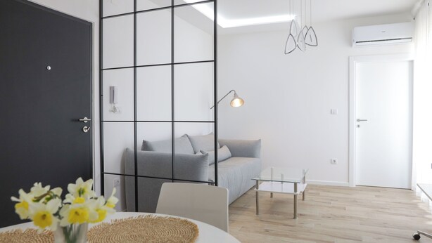A modern living room with a grey sofa, a white coffee table, and a glass partition.