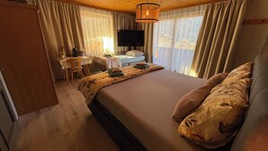 Ein Schlafzimmer mit einem großen Bett, einem Schreibtisch mit Stuhl, einem Fernseher und Vorhängen.