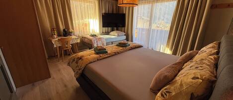 A bedroom with a large bed, a desk with a chair, a television, and curtains.