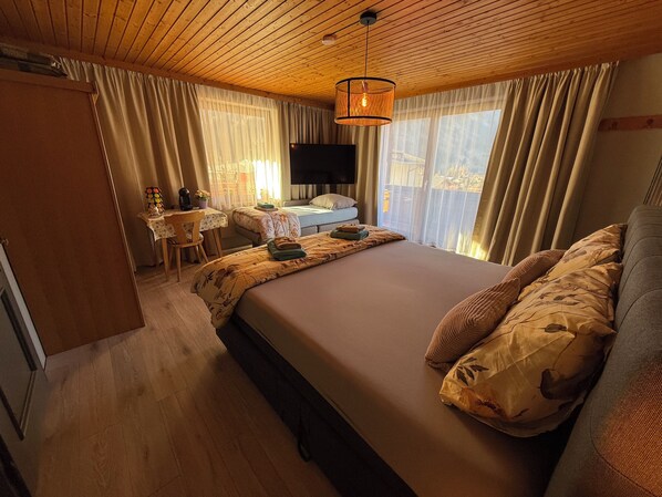 A bedroom with a large bed, a desk with a chair, a television, and curtains.