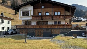 Eine zweistöckige Chalet mit Holzbalkon, Stein Fundament und Blick auf eine Berglandschaft.