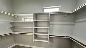 A walk-in closet with built-in shelves and a ladder, grey walls, and wooden flooring.