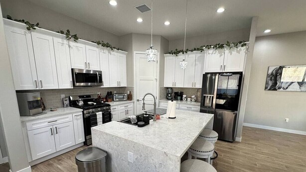 A modern kitchen with white cabinets, stainless steel appliances, and a marble island with bar stools.