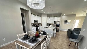 A modern kitchen with white cabinets, a central island, and a dining area with a wooden table and chairs.