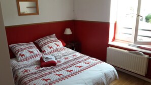 Ein Bett mit gemusterten Bettbezügen, eine Nachttischlampe, ein Spiegel an der Wand und ein Fenster mit Blick nach draußen.