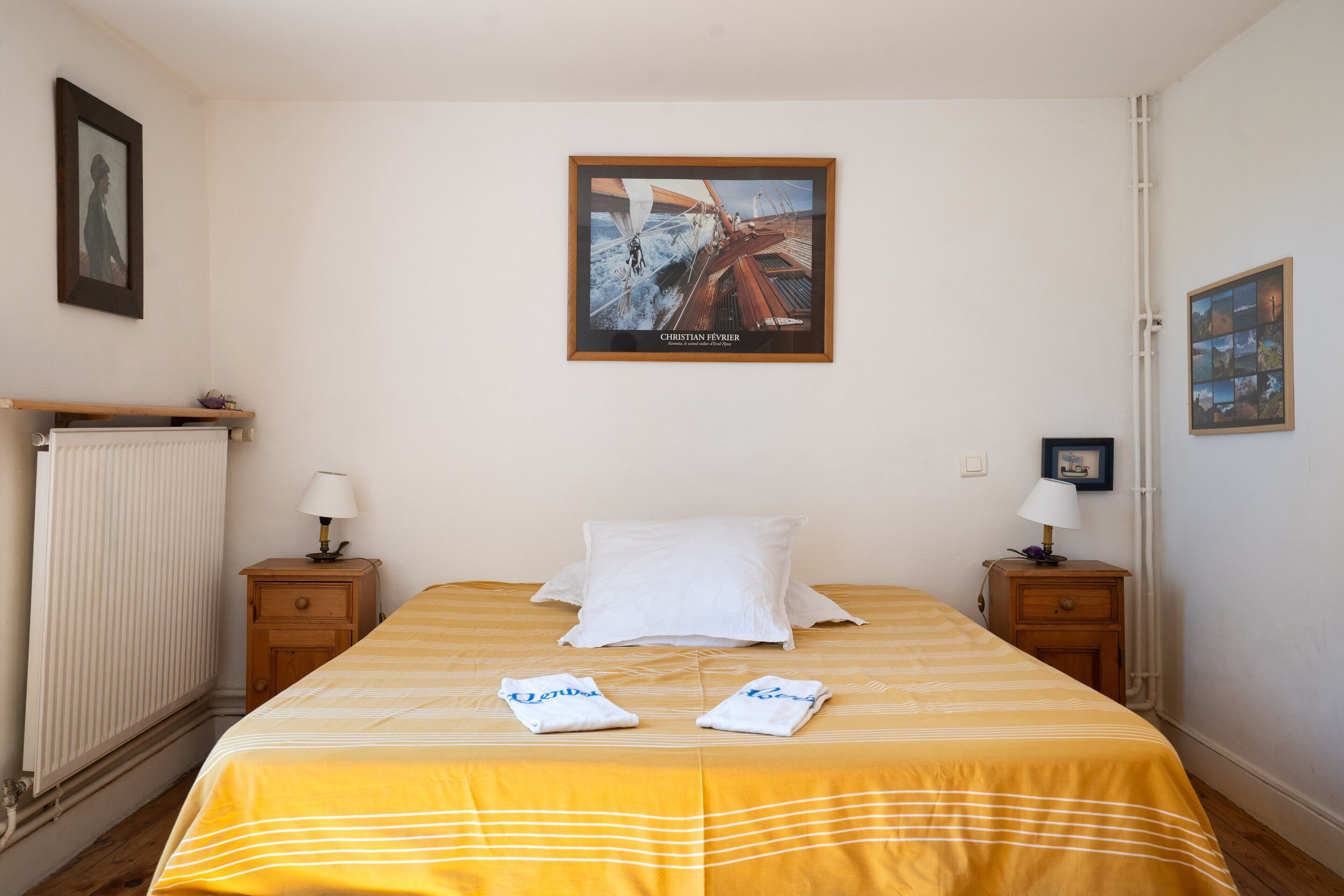 Een hotelkamer met een bed, twee nachtkastjes, een radiator en een lijst aan de muur.