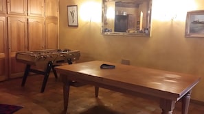 A room with a foosball table, a long wooden table, and a mirror on the wall.