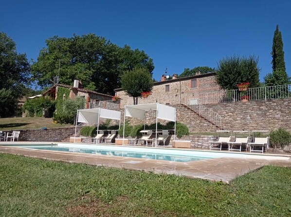 A pool area with lounge chairs and umbrellas, a stone building with a staircase, and greenery in the background. - San Domenico. 6 bedrooms, 6 bathrooms, private pool (Arezzo)