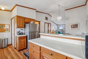 A kitchen with wooden cabinets, a stainless steel refrigerator, a white countertop, and a chandelier. - New for 2026!  Semi OF Townhouse in Kitty Hawk (Kitty Hawk)