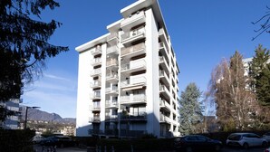 Un edificio residenziale a più piani con balconi, un'area di parcheggio e una vista chiara sulle montagne sullo sfondo.