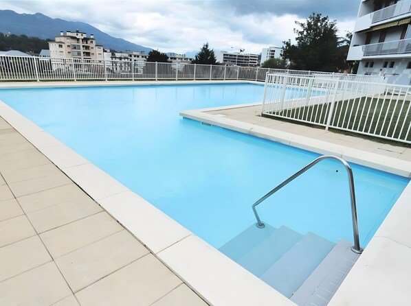 Ein Schwimmbecken mit Metallleiter und weißen Geländern, umgeben von einem weißen Zaun.