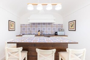 A kitchen with a central island, white chairs, a tiled backsplash, and overhead lighting. - Gardenia- 03 bedroom villa with private Jacuzzi (Massa Lubrense)