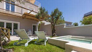 Et moderne udendørsområde med pool, to liggestole og et pergolaoverdækket område.
