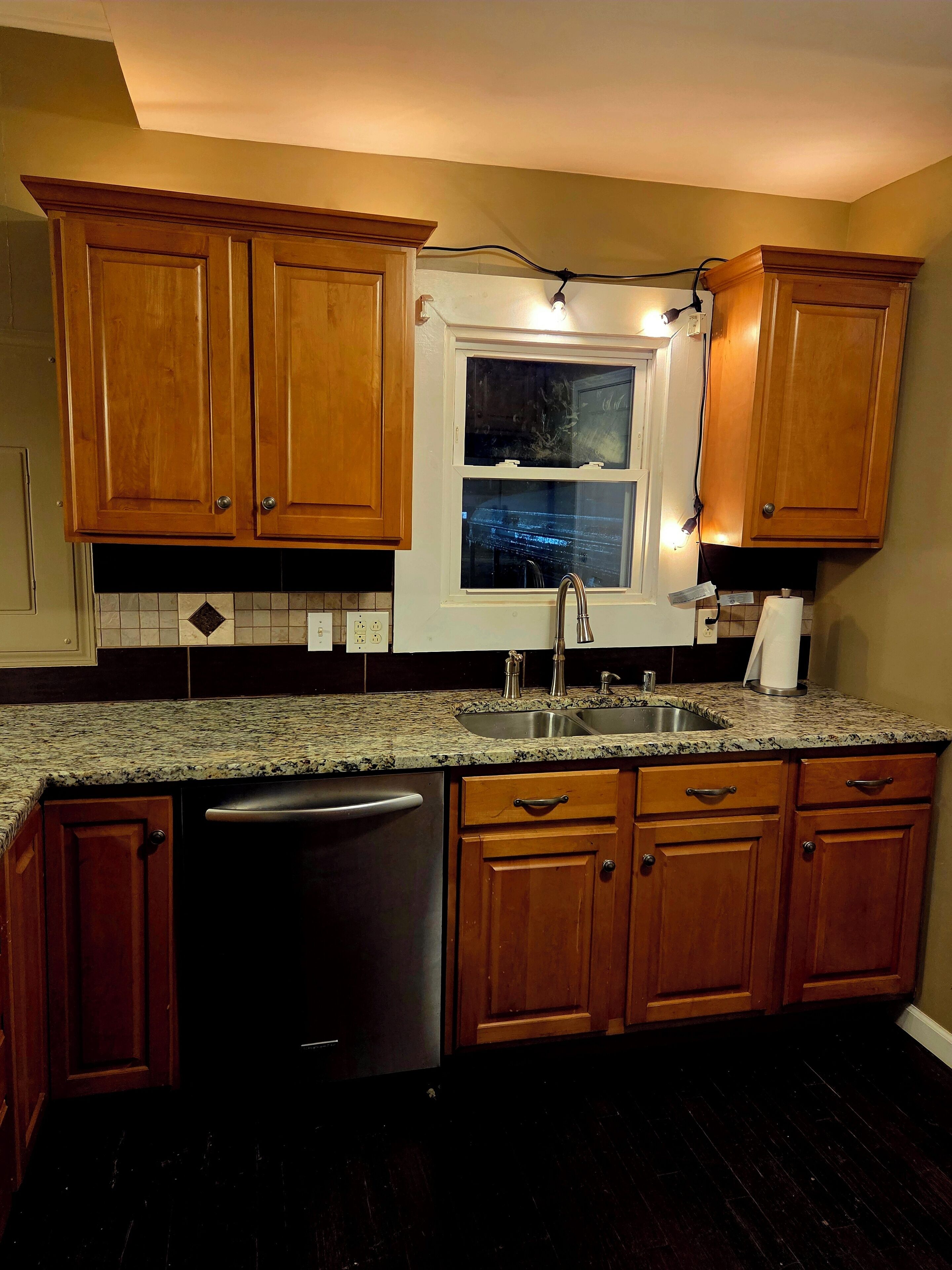 A kitchen with wooden cabinets, a granite countertop, a stainless steel sink, and a dishwasher.